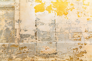 Texture detail of peeling paint and stucco in beige and yellow tones.