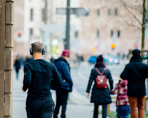 Rear view of unrecognizable people in city - man running with headphones and pedestrians discovering modern city