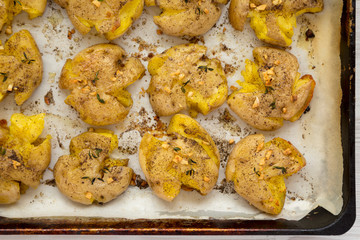 Homemade garlic thyme smashed potatoes on a baking sheet, top view. Flat lay, overhead, from above. Close-up.