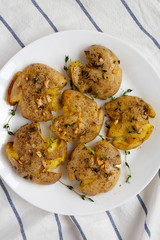 Homemade garlic thyme smashed potatoes on a white plate, top view. Flat lay, overhead, from above. Close-up.