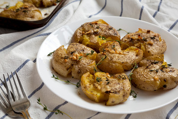 Homemade garlic thyme smashed potatoes on a white plate, side view. Close-up.