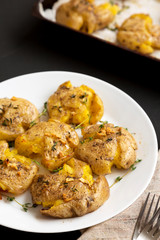 Homemade garlic smashed potatoes on a white plate on a black background, side view. Close-up.