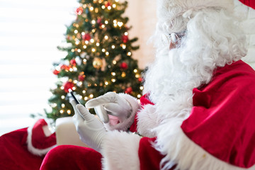 Fototapeta na wymiar Man in Santa costume using smart phone at home