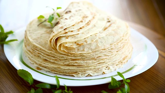 many fried thin pancakes in a plate, on a table.