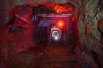 Dark dirty abandoned uranium mine with rusty remnants of railway color illuminated - obrazy, fototapety, plakaty
