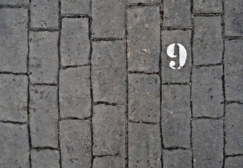 9, number nine, white stencil number on cobblestone surface.