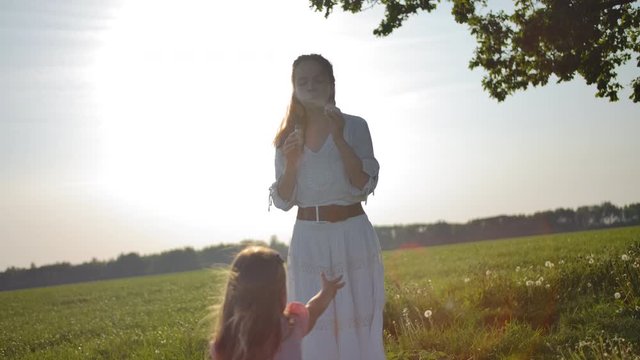 Mom in a white dress blows soap bubbles for her little daughter