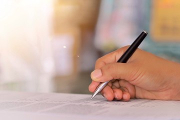 A woman's hand holding a pen to write or sign an autograph on paper.
