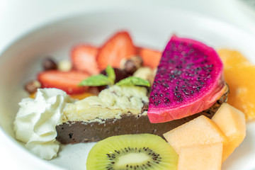 Traditional homemade chocolate cake with mix fruit sweet pastry dessert on white disc.