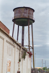 An old, unkept water tower is left to rust above an abandoned industrial complex.