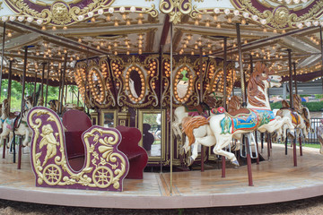A classically themed retro styled children's carousel with horses and mirrors amusement park outdoor mechanical ride (merry go round) sits unused on a summer day.