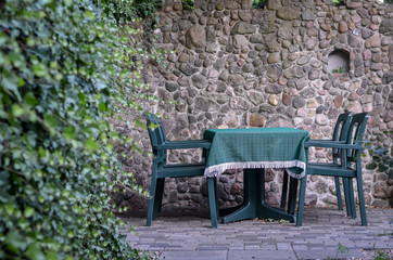 Green table and chairs on the background of stone wall in cozy outdoor terrace