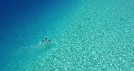 Aerial view of young couple snorkeling in pristine blue turquoise water on a sunny sparkling day, amazing lagoon adventure
