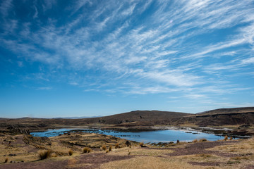 Fototapeta na wymiar The thin whips strands of the Cirrus clouds create a beautiful contrasting backdrop to the dry, brown grass surrounding the wetlands of Sillustani in Peru