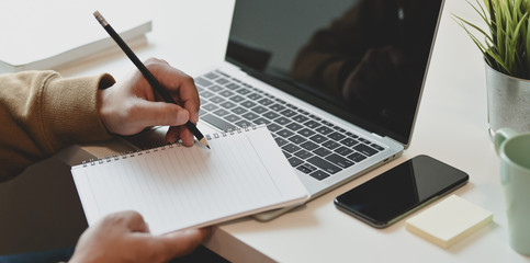 Fototapeta premium Close-up view of male freelancer writing his idea ion notebook in comfortable room