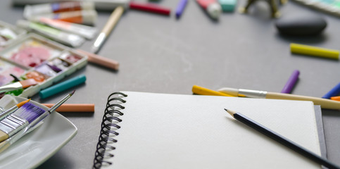 Professional artist workplace with water colours, soft pastel colours and painting brushes with blank notebook