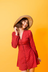 Powerful girl in red dress wearing hat posing relax in orange background