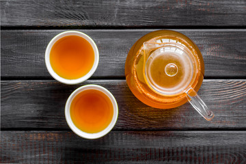 Cups and teapot with brew on wooden background top view