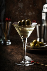 Martini vodka cocktail, with dry vermouth, vodka and green olives, bar tools, vintage wood counter, selective focus