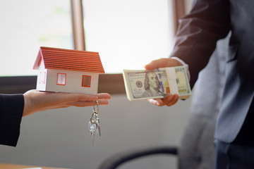 Agents are giving house keys of customer and holding dollar us bank at agency office. Agreement concept.
