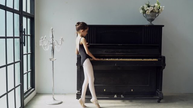4K Tracking shot happy little child girl dancer in black leotard and ballet slipper shoes jumping and dancing contemporary ballet dance practice at vintage studio room. Young girl dancing in the room.