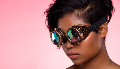 Tanned Skin Teenager Fashion Model looks at camera for shooting new collection Sunglasses.  Beautiful Asian Woman trend make up wear Kaleidoscope Glasses with colorful, studio lighting pink background