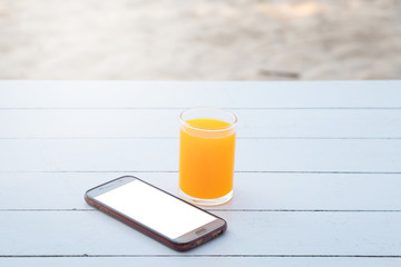 Orange juice in glass and mobile phone on white wooden table