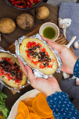 Woman hands holds baked stuffed potatoes with vegetables in foil. Homemade vegan food. 