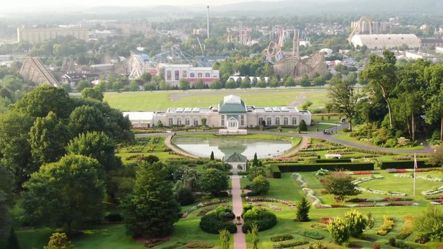 Rising aerial shot of a beautiful manicured garden with amusement theme park in distance, recreation, tourism, travel theme