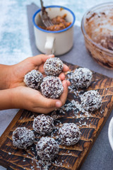 Little girl hands holds coconut sweet balls. Energy protein dessert with dates, cocoa, peanut butter.