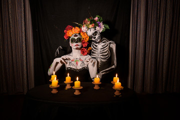 Clown with flowers on head and skeleton with candles together in the dark night, Mexico.