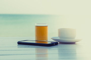 Tea coffee with smart phone on the white wooden table at the beach