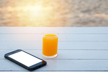 Orange juice in glass and mobile phone on white wooden table