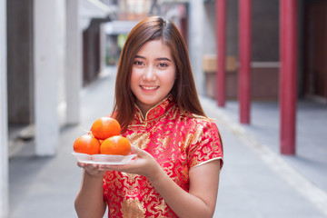 The girl wears a cheongsam costume, holding oranges. Oranges are auspicious fruit used for blessings during the Chinese New Year.