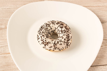 Fresh glazed donut with chocolate sprinkles on a white plate.
