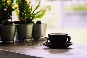 Coffee cup and reading glasses on cement table with nature background