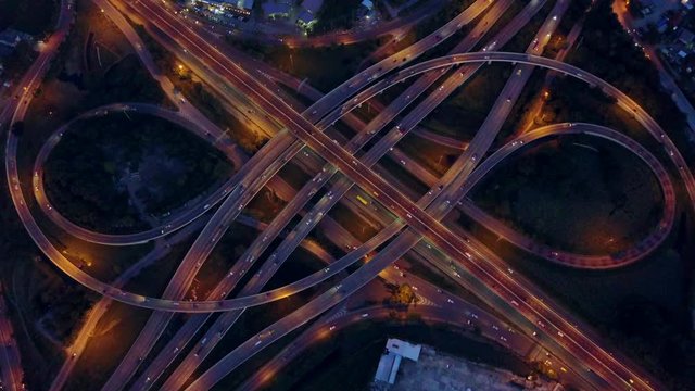 4K. Aerial view of road interchange or highway intersection with busy urban traffic speeding on the road at night. Junction network of transportation taken by drone.