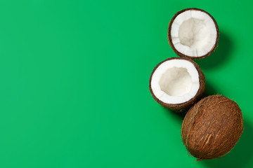 Whole and cracked coconuts on green background. Top view.