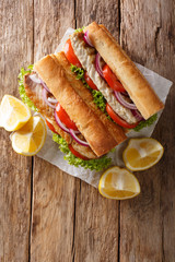 sandwich balik Ekmek with grilled fillet of mackerel, tomatoes, onions and lettuce served with lemon closeup on the table. Vertical top view