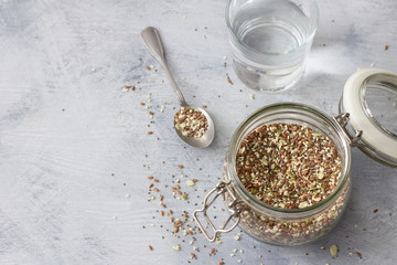 Cereal mixture for healthy keto crackers of chia seeds, flax, sesame, ground pumpkin seeds in a glass jar on a gray wooden background, horizontal