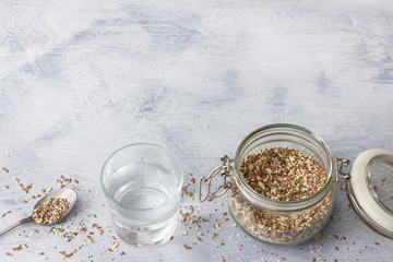 Obraz na płótnie Canvas Cereal mixture for healthy keto crackers of chia seeds, flax, sesame, ground pumpkin seeds in a glass jar on a gray wooden background, horizontal