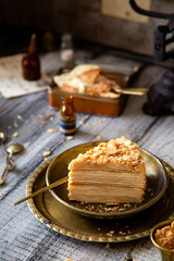 tasty slice of homemade creamy layered traditional russian cake napoleon on vintage gold metal plates on grey wooden table with old scales