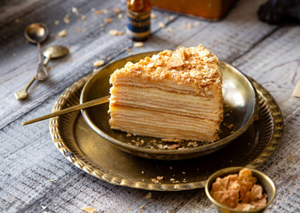 tasty slice of homemade creamy layered traditional russian cake napoleon on vintage gold metal plates on grey wooden table with old scales