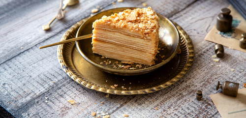 tasty slice of homemade creamy layered traditional russian cake napoleon on vintage gold metal plates on grey wooden table with old scales