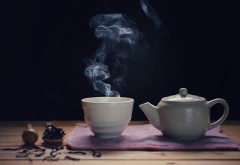 a cup of hot tea with tea pot , hot smoke, dark background.