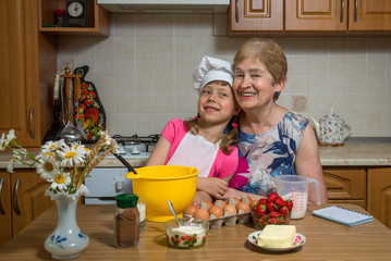 Grandmother and little granddaughter prepare the dough for the cake.