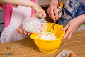 Grandmother and little granddaughter prepare the dough for the cake.
