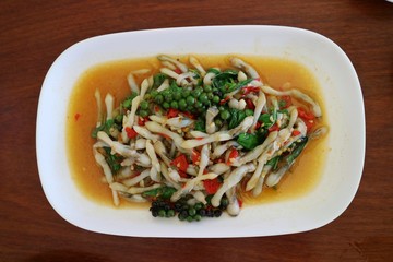 Spicy stir fried Razor clam with pepper and thai herb in white dish on wooden table. Thai food concept.