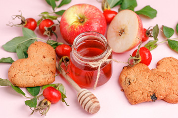 Ingredinets for winter fall autumn seasonal beverage tea party - fresh rose hip berries, honey, apple and heart-shaped biscuits. Concept of cozy teaparty witn immunity drink