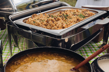 Close-up appetizing pilaf with gravy chicken beef serving for buffet food at luxury hotel. Hot fresh meal lunch or dinner in steel food dish ready for smorgasbord